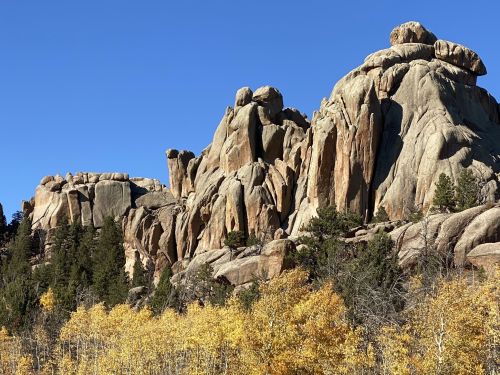 Rocky formations rise against a clear blue sky, surrounded by vibrant autumn foliage.