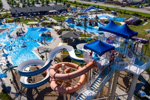 Aerial view of a vibrant water park featuring slides, pools, and sunbathing areas with umbrellas and people enjoying the water.