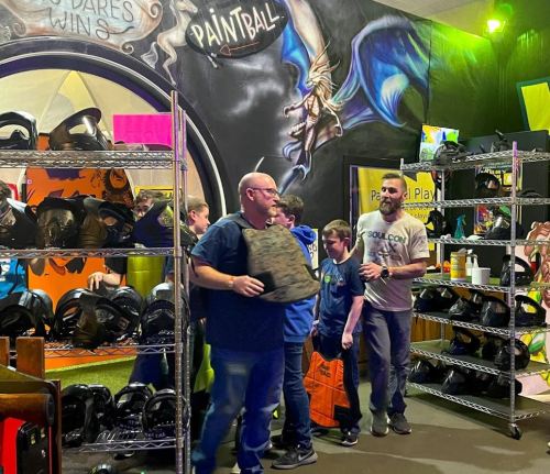 A group of people in a paintball facility, preparing gear and interacting in a colorful, vibrant environment.