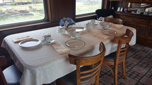A dining table set with plates, cups, and a floral centerpiece, surrounded by wooden chairs in a cozy room.