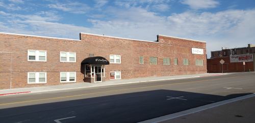 A brick building with large windows and a black awning, set against a blue sky with scattered clouds.