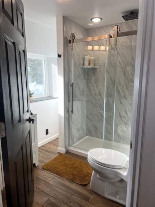 Modern bathroom featuring a glass shower, marble walls, a toilet, and a window with natural light.