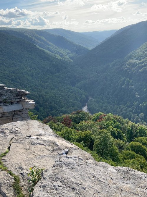 A scenic view of a lush green valley surrounded by mountains under a bright sky, with a river winding through the landscape.