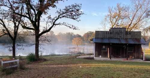 A rustic cabin by a misty lake, surrounded by trees and a serene landscape at dawn.