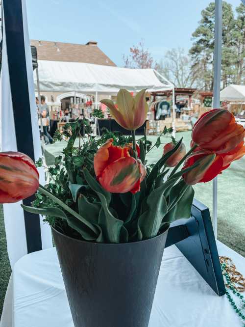 A bouquet of orange and yellow tulips in a black vase, set against a blurred outdoor market scene.