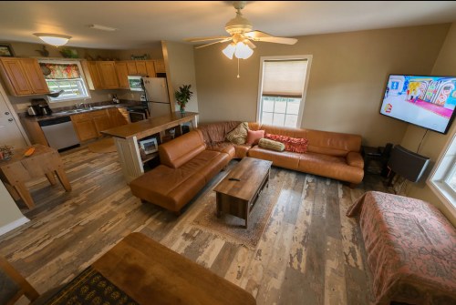 A cozy living room with a brown leather sofa, wooden coffee table, and a TV, featuring a kitchen in the background.
