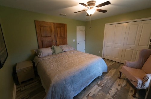 Cozy bedroom with a green wall, a queen bed, wooden closet doors, and a pink armchair in the corner.