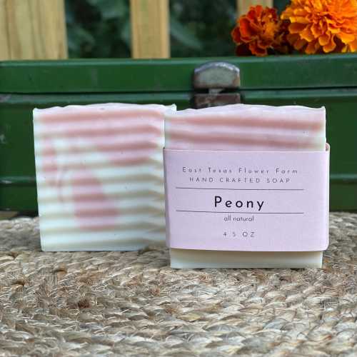 Two bars of pink and white marbled soap labeled "Peony" on a natural fiber surface, with a green background.