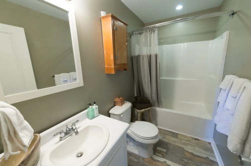 A clean bathroom featuring a shower, toilet, sink, and wooden accents with towels hanging on the wall.