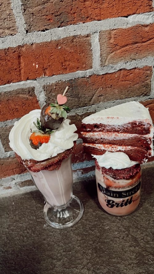 A milkshake topped with whipped cream and a cherry, alongside a slice of red velvet cake with cream cheese frosting.