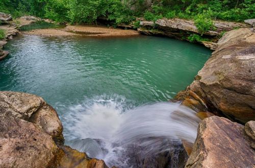 A serene waterfall cascading into a turquoise pool surrounded by lush greenery and rocky cliffs.