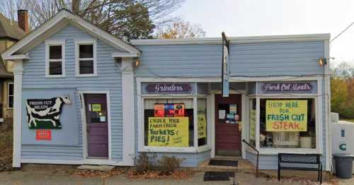 A small blue building with signs for fresh cut meats and pies, featuring large windows and a welcoming entrance.