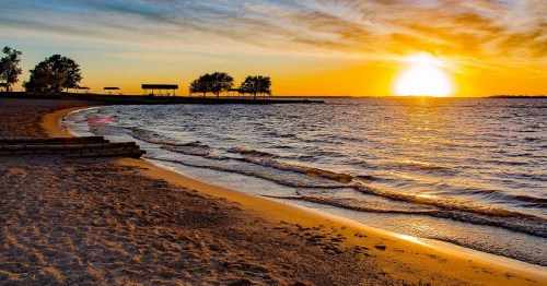 A serene beach at sunset, with gentle waves lapping at the shore and trees silhouetted against the colorful sky.