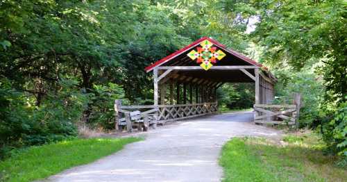 A scenic view of a covered bridge surrounded by lush greenery and a pathway leading through the trees.