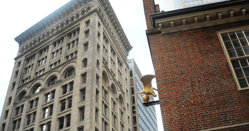 A tall, historic building with ornate architecture next to a brick building featuring a golden eagle sign.