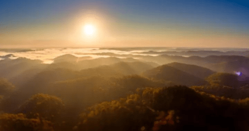 A breathtaking sunrise over misty mountains, with soft light illuminating the landscape and creating a serene atmosphere.