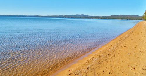 A serene beach scene with clear water gently lapping at a sandy shore under a bright blue sky.