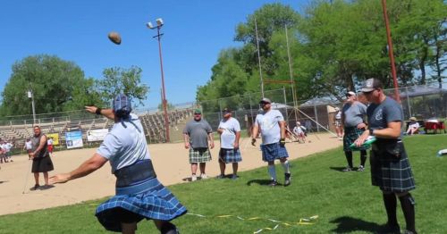 A group of men in kilts compete in a field event, throwing a heavy stone at a sports festival.