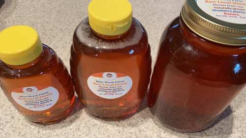 Three jars of honey with yellow lids, varying in size, placed on a countertop. Labels indicate they are raw honey.