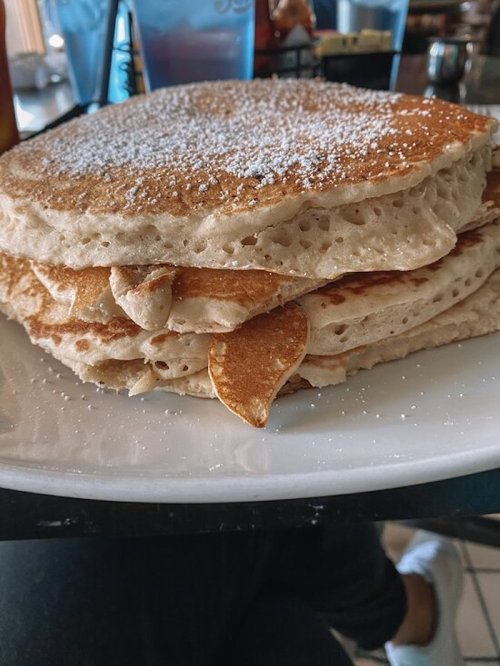 A stack of fluffy pancakes dusted with powdered sugar on a white plate.
