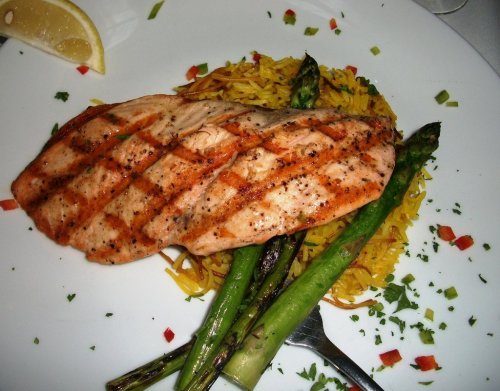 Grilled salmon fillet on a bed of yellow rice, garnished with asparagus and lemon wedges.