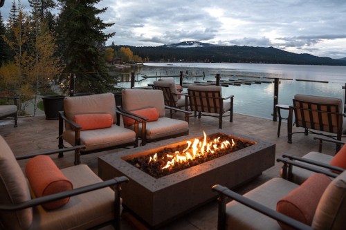 Cozy outdoor seating area with a fire pit overlooking a lake and mountains at dusk.
