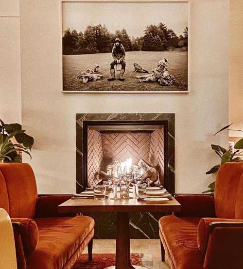 Cozy dining area with two chairs, a table set for dinner, and a fireplace beneath a large framed photo.