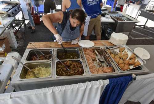 A woman serves food from a buffet table with various dishes at an outdoor event.