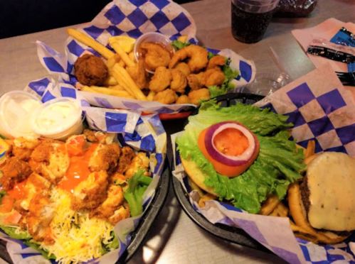 Three plates of food featuring fried shrimp, chicken salad, and a burger with lettuce and tomato, served with fries.