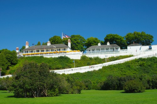 A historic building on a hillside, surrounded by greenery and a clear blue sky, with an American flag flying.