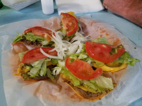A plate of tacos topped with lettuce, tomatoes, onions, and cheese, served on parchment paper.