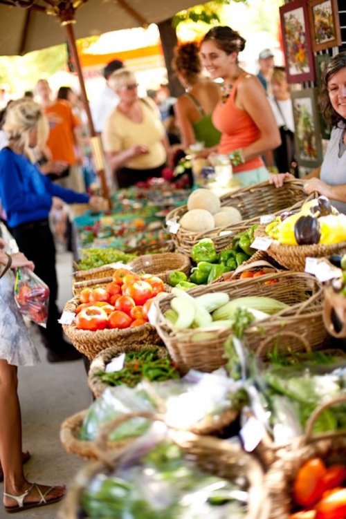 A bustling farmers market with people browsing colorful baskets of fresh fruits and vegetables.