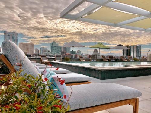 Rooftop pool area with lounge chairs, umbrellas, and a city skyline under a cloudy sky.