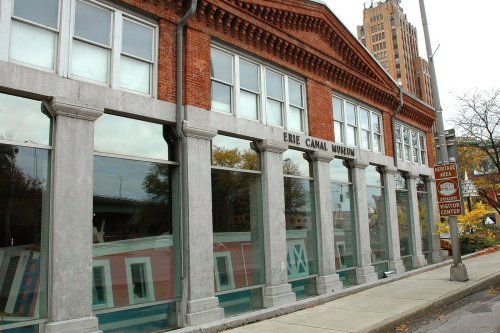 Exterior of the Erie Canal Museum, featuring brick architecture and large windows, with nearby signage.