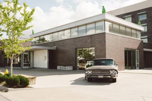 A vintage car parked in front of a modern building with large windows and green sculptures on the roof.