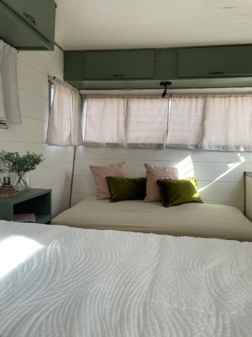 Cozy interior of a small bedroom with a bed, decorative pillows, and soft natural light filtering through curtains.