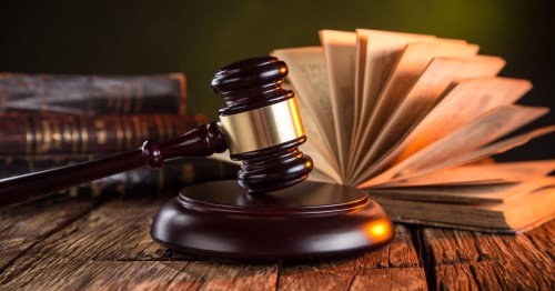 A wooden judge's gavel resting on a sound block with an open book and stacks of old law books.