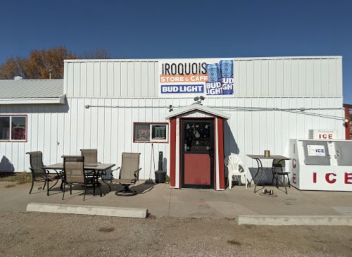 Exterior of Iroquois Store & Café with outdoor seating, a sign for Bud Light, and an ice vending machine.