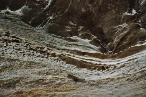 Textured rock surface with wavy patterns and subtle color variations, resembling natural erosion and geological formations.