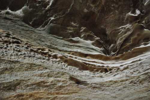 Textured rock surface with wavy patterns and subtle color variations, resembling natural erosion and geological formations.