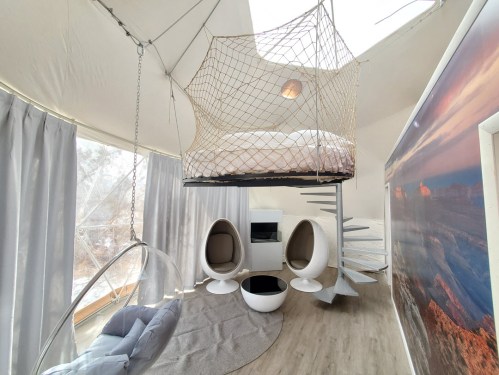 A modern, cozy interior featuring a hanging bed, spiral staircase, and unique seating in a tent-like space.