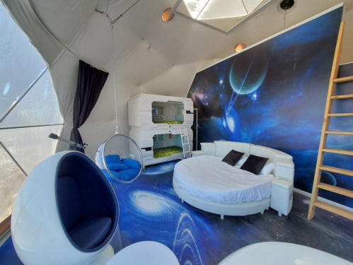 Futuristic interior of a geodesic dome with a round bed, bunk beds, and space-themed decor.