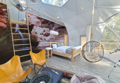 Cozy interior of a geodesic dome with a bed, hanging chair, and natural decor featuring rock formations.