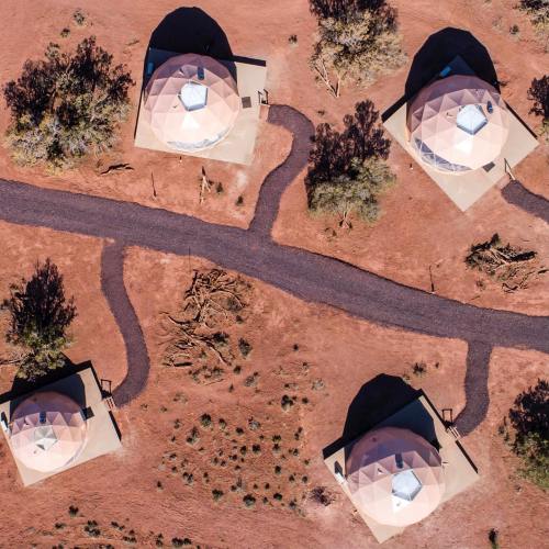 Aerial view of four dome-shaped structures on red earth, surrounded by sparse vegetation and winding pathways.