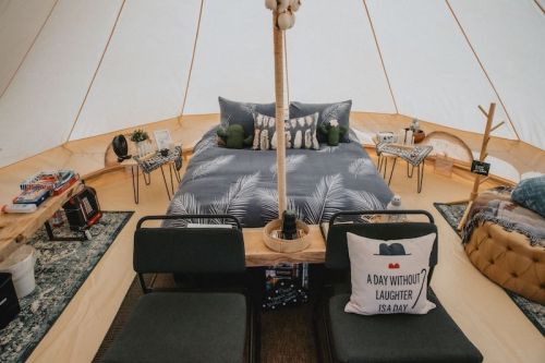 Cozy glamping tent interior with a bed, seating area, and decorative pillows, surrounded by natural elements.