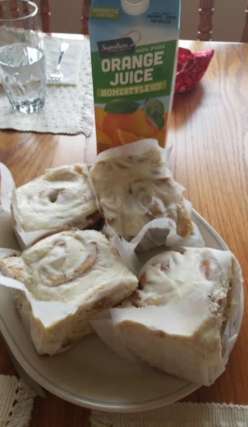 A plate of cinnamon rolls with cream cheese frosting next to a carton of orange juice on a wooden table.