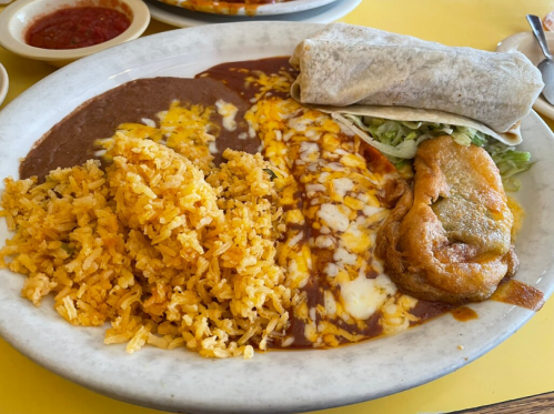 A plate of Mexican food featuring rice, refried beans, a burrito, cheese, and a stuffed pepper.