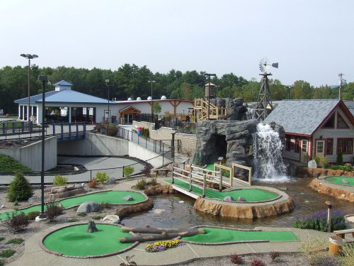 A mini-golf course with waterfalls, surrounded by buildings and greenery on a clear day.