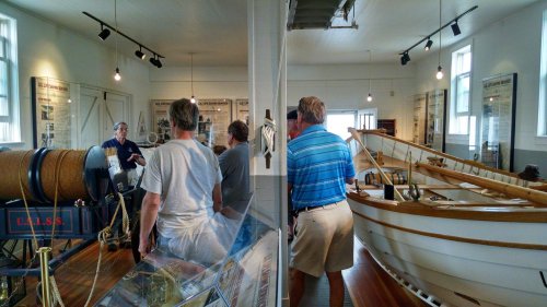 Visitors explore a maritime museum, admiring exhibits and a wooden boat in a well-lit, spacious gallery.
