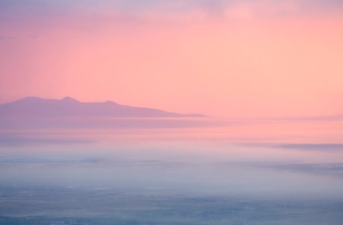 A serene landscape featuring soft pink hues in the sky above a distant mountain range and calm waters.